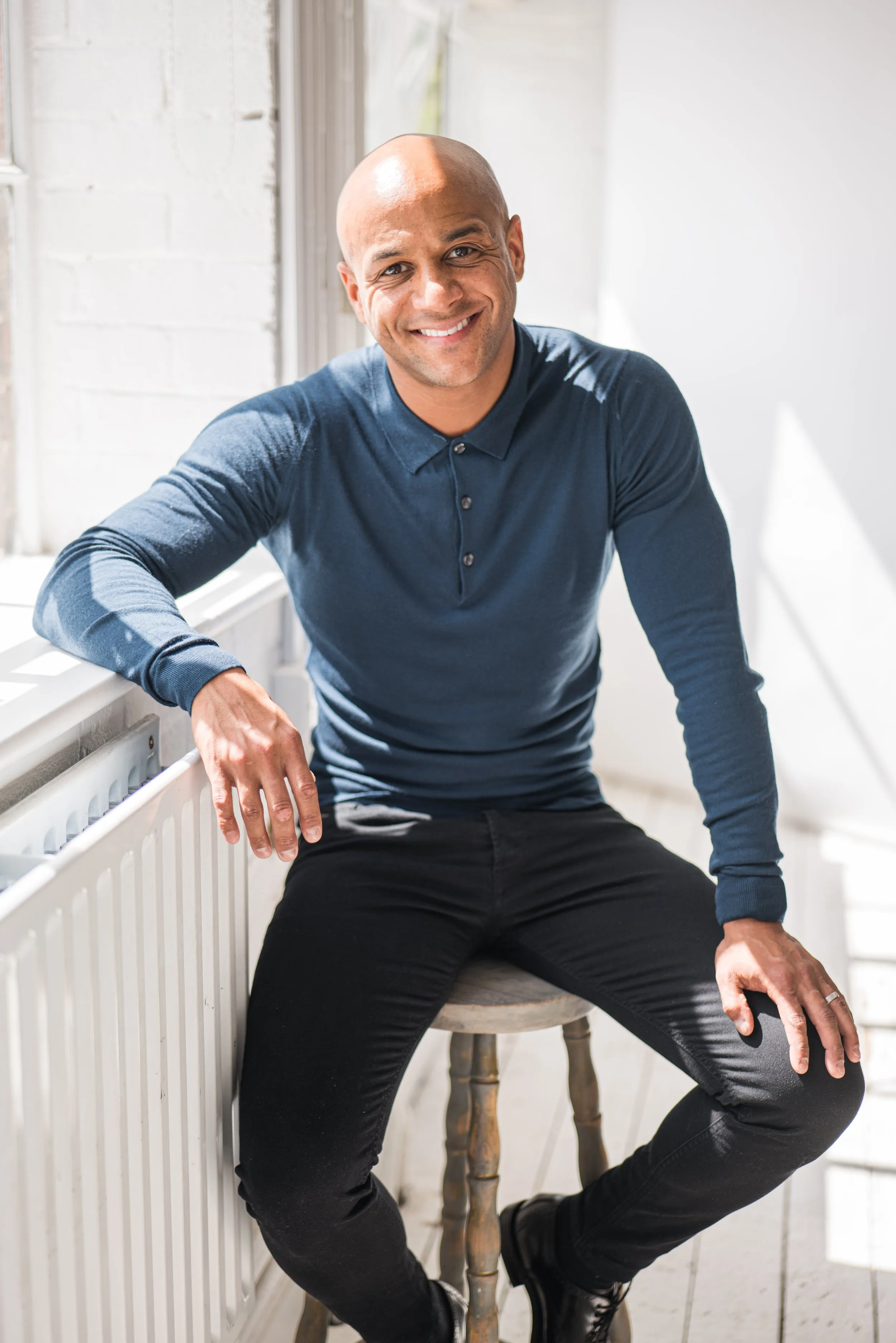 Relaxed corporate headshot of bald man in blue polo seated in natural light, London