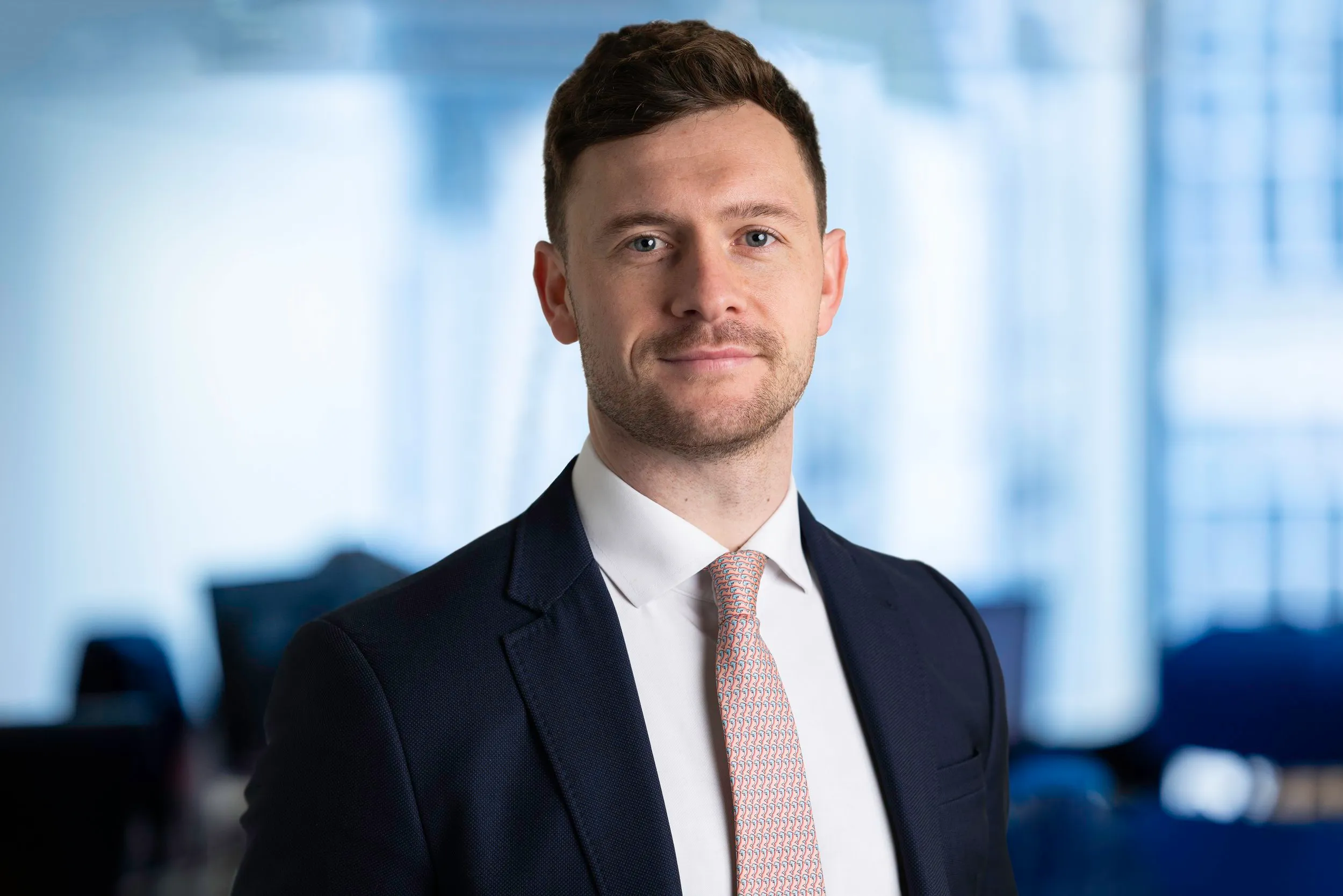 Corporate headshot of man in navy suit with pink tie, office background, London