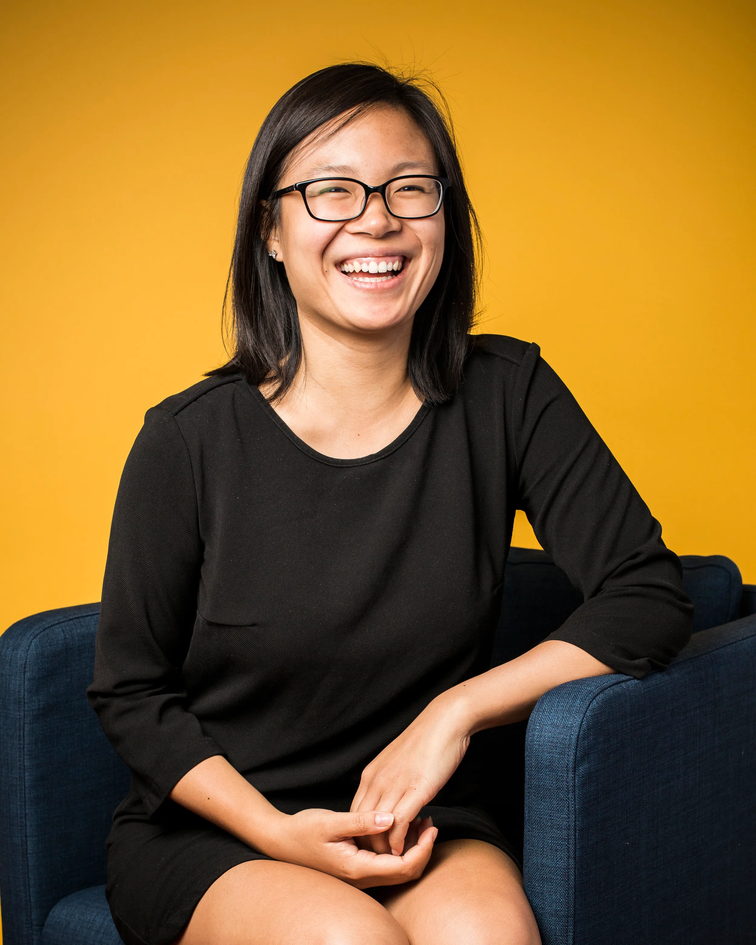 Creative professional headshot of woman in glasses and black dress, yellow background, London
