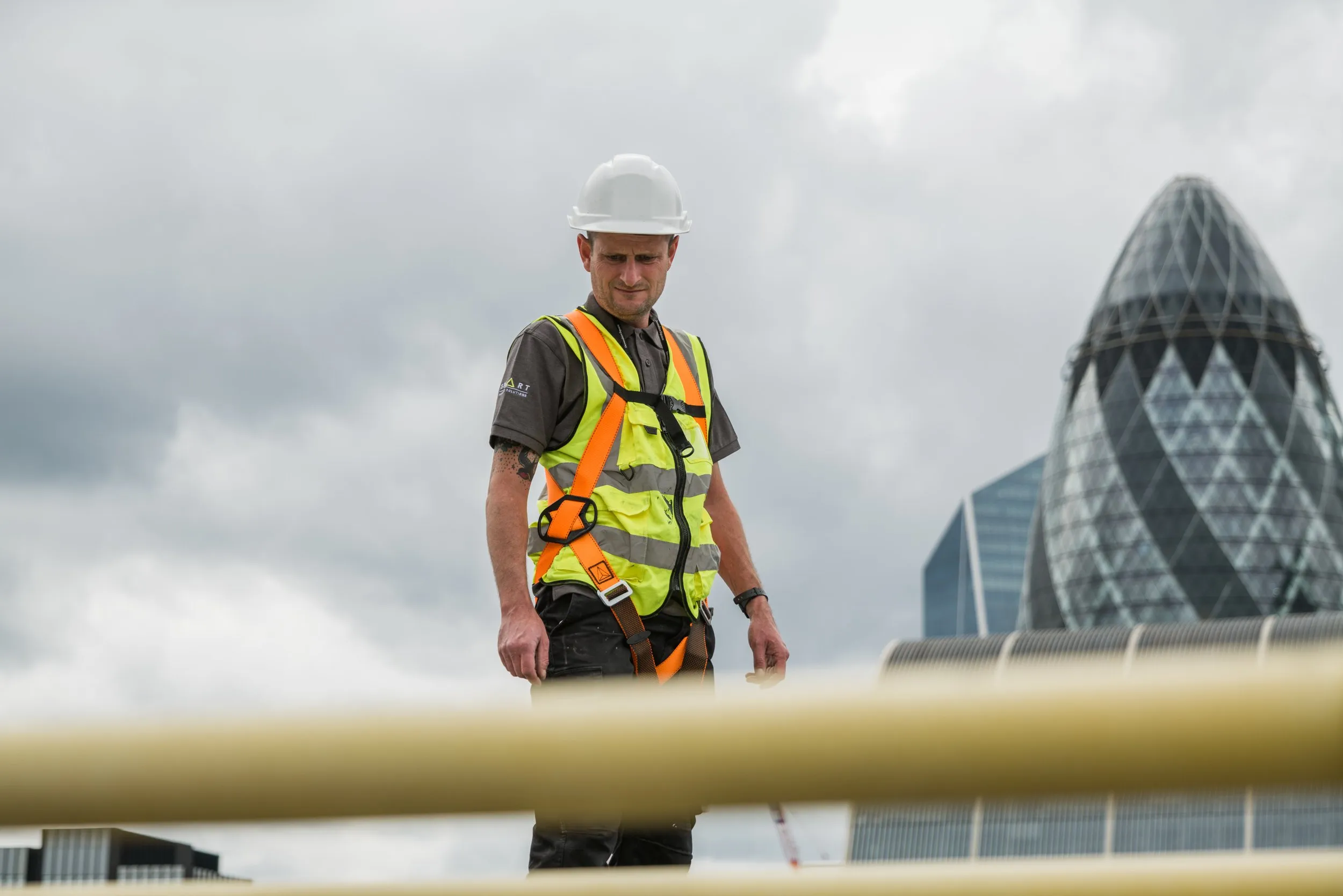 Engineer on rooftop in hi-vis vest with Gherkin and City of London skyline, corporate photography